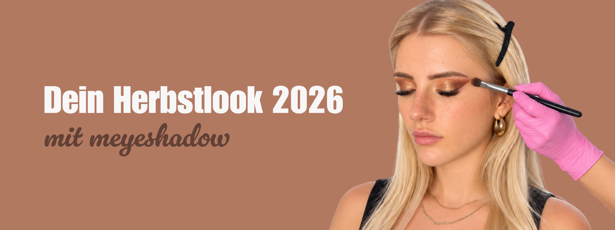 Herbstlook 2026 mit meyeshadow: Blonde Frau mit warmem braunem Augen-Make-up und Lidschattenpinsel vor rosébraunem Hintergrund